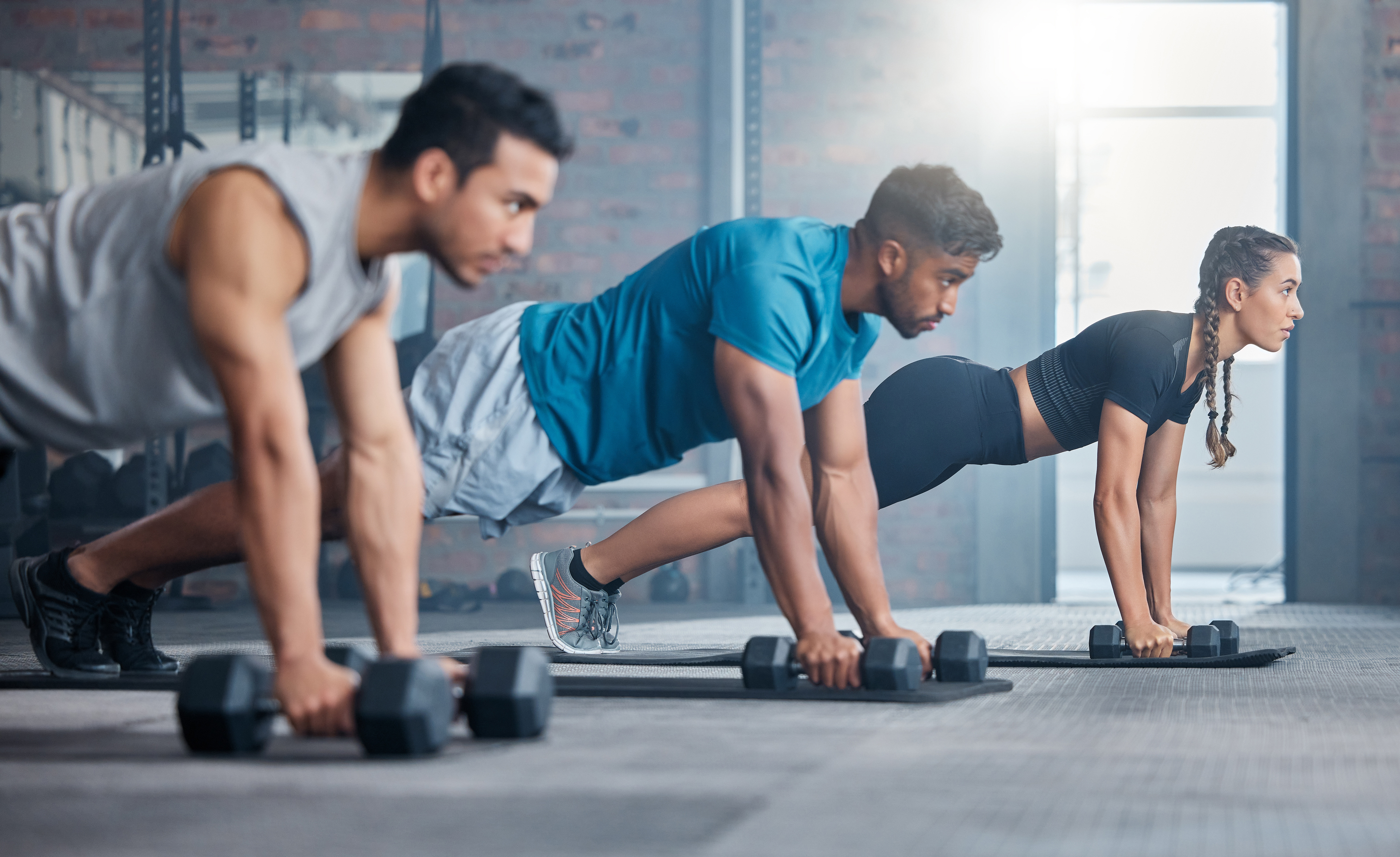Group, workout and dumbbell push up at gym for muscle, power or strength. Teamwork, sports or energy of people, athletes or bodybuilder friends exercise or training at fitness center for healthcare